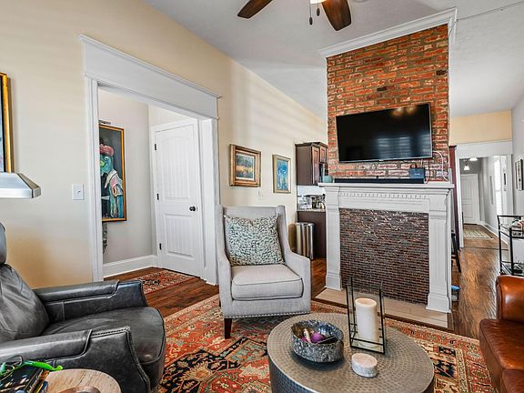 Warm and welcoming, the living room boasts an exposed brick decorative fireplace, soaring ceilings, and hardwood floors