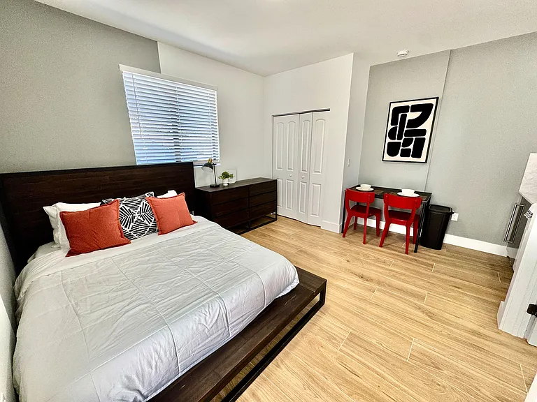 Furnished bedroom featuring a full bed, dresser, and a compact dining/work table, plus a closet and window blinds.