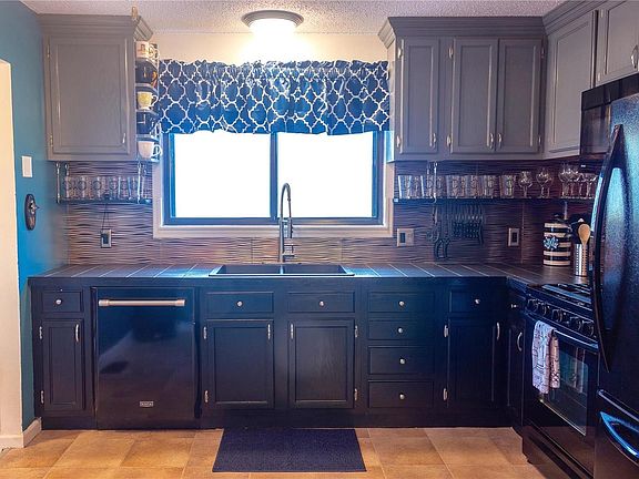 Updated kitchen boasts custom cabinets, tile countertop, stainless backsplash, new fixtures, gas oven/range, and a breakfast bar