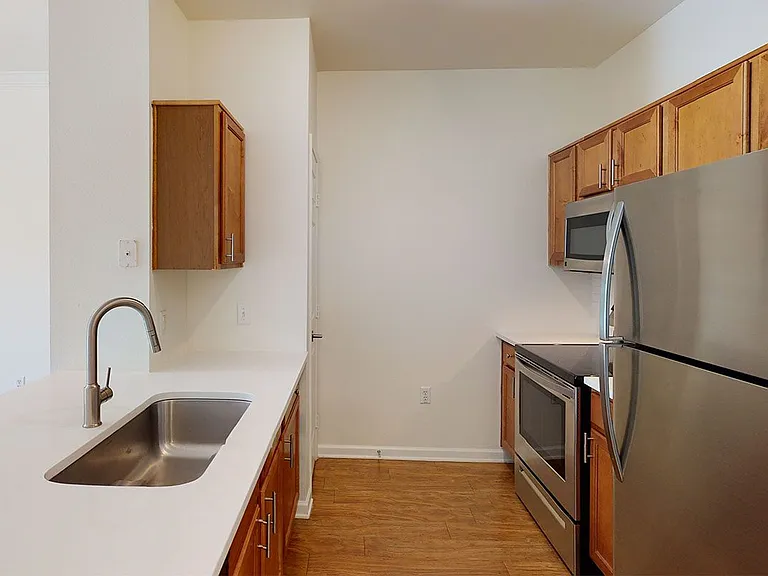 Apartment kitchen with stainless steel appliances and wood-style flooring. Quartz-style countertops (shown here) are available in select homes.
