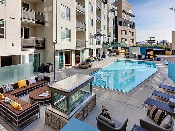 Swimming pool surrounded by poolside cabanas, lounge chairs and tables, and an outdoor fireplace.