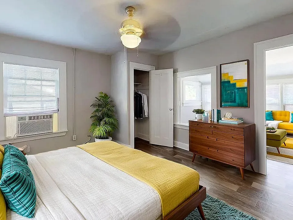 Charming bedroom with modern decor, vibrant teal and yellow accents, leading to a stylish living area with a bright yellow sofa.