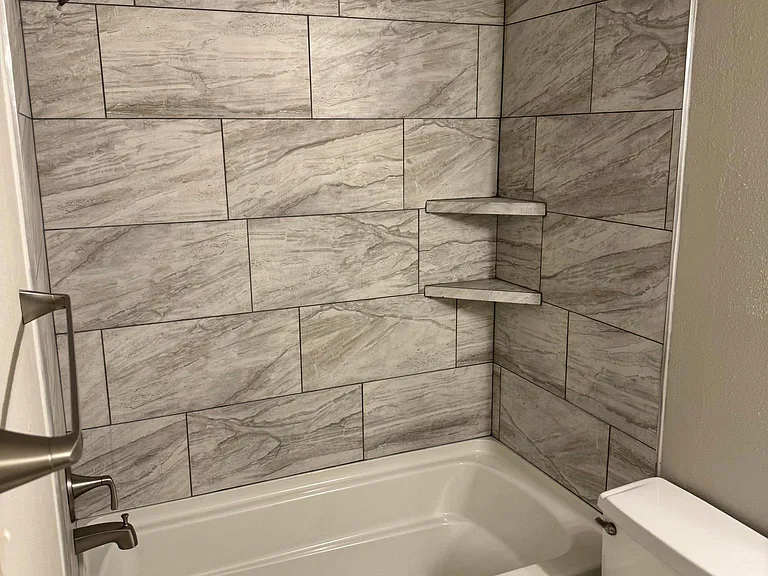 Bathroom features bath tub with tile walls with shelves.