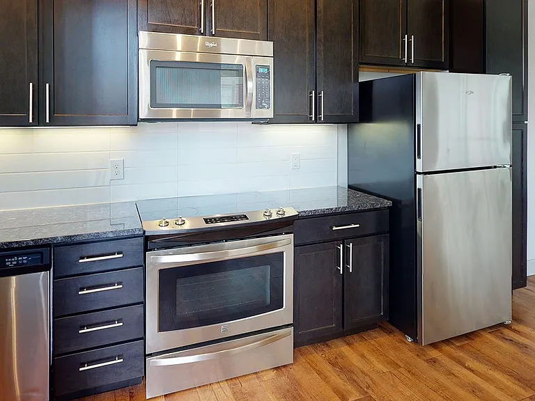 Apartment kitchen with stainless steel appliances, granite countertops and wood-style flooring.