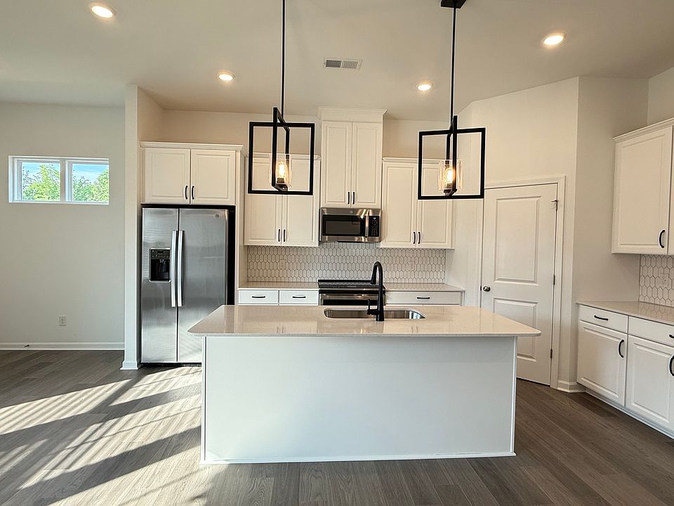 Chef's kitchen featuring quartz countertops, a large center island, stainless steel GE appliances, and designer lighting.
