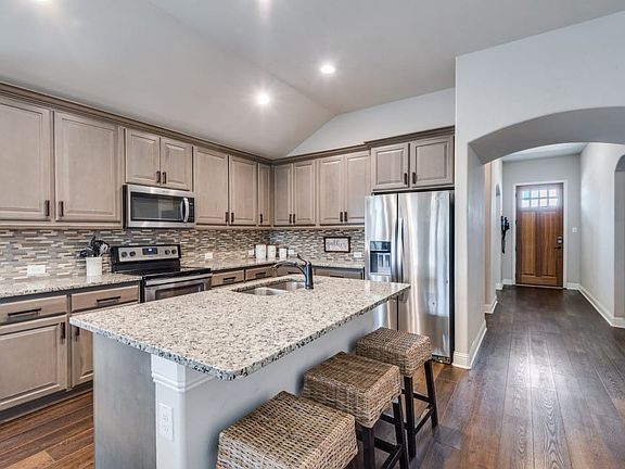 Kitchen featuring a large island with stone countertops, stainless steel appliances, extensive cabinetry, and a mosaic tile backsplash