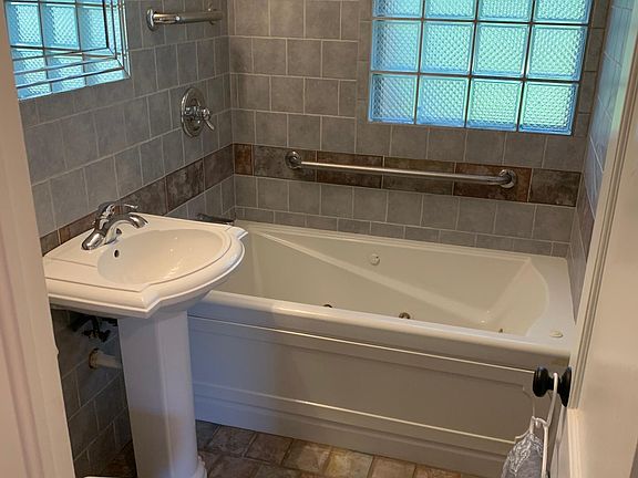 Bathroom features Jacuzzi tub, pedestal sink, and tile surround and floor.