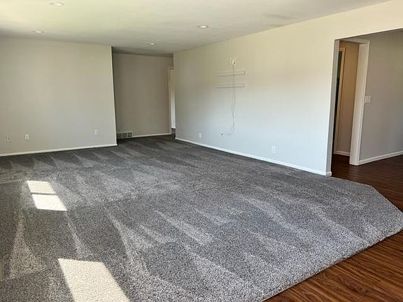Large carpeted living room space that connects the entryway, kitchen dining and bedrooms