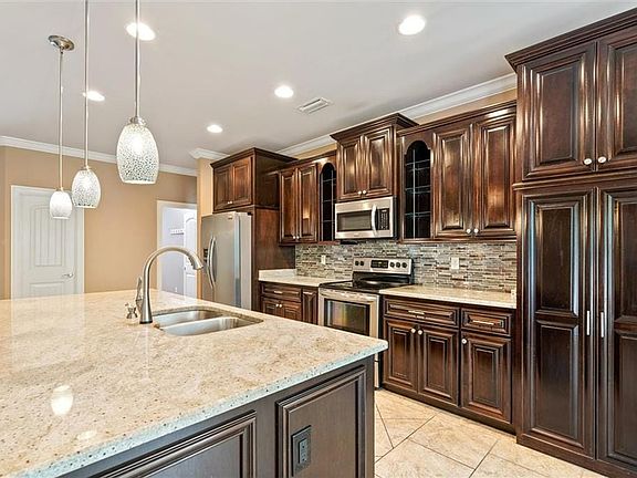 Kitchen with dark brown cabinets, appliances with stainless steel finishes, a kitchen island with sink, sink, and decorative light fixtures