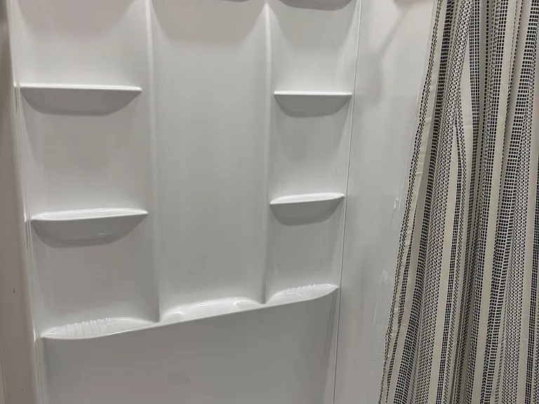 Walk-in shower with a fixed showerhead, built-in corner shelving, and an easy-care surround.