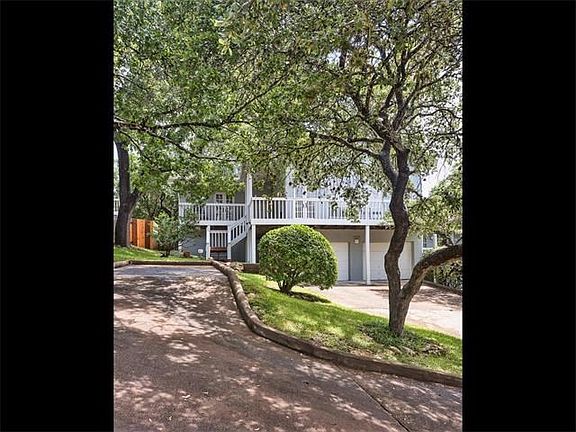 Spacious two car garage with an additional parking area to the left.  Beautiful trees frame this lovely cottage style On the ground level, there is a spacious two car garage with additional parking to the left.  Beautiful trees surround the condo and add 