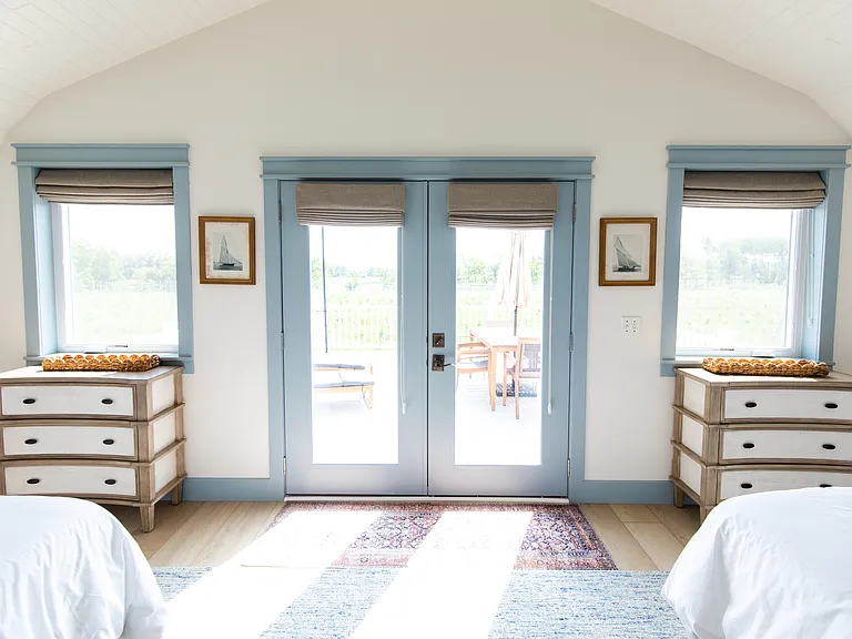 The second bedroom includes two full beds, two small dressers, a closet, a desk, and French doors that open out to the expansive back deck that overlooks vineyards.