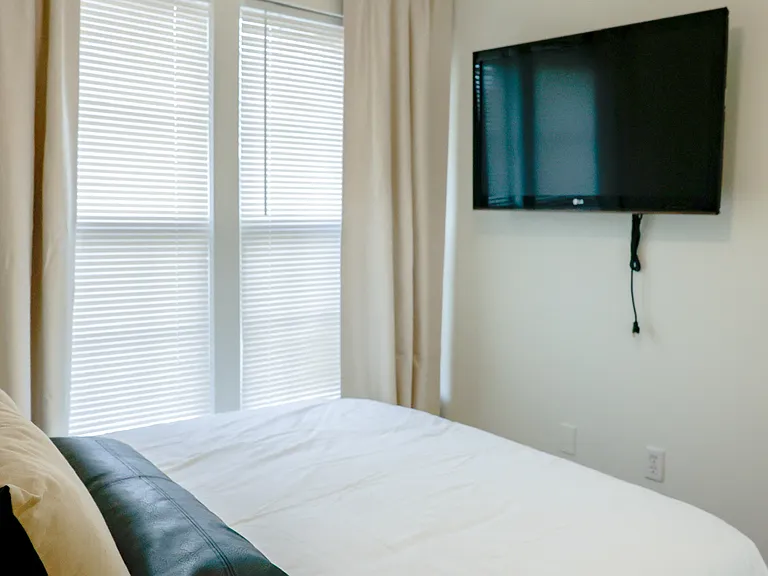 Bright bedroom featuring large windows for natural light and a professionally mounted smart TV with 4K Firestick for modern convenience.