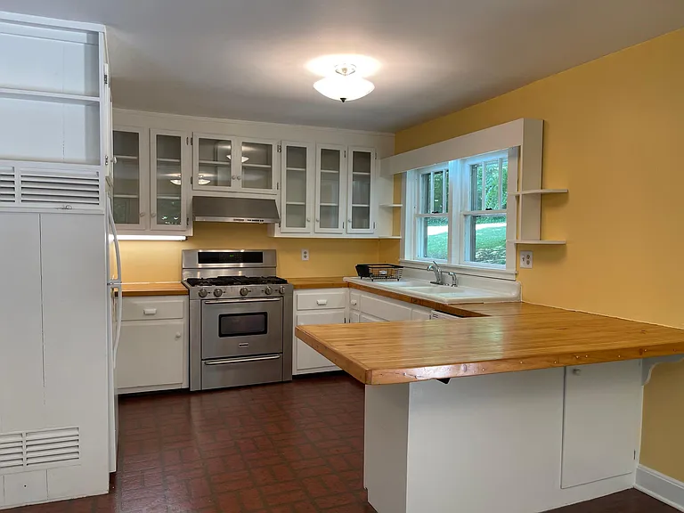 A spacious kitchen with newly refinished butcher block counters, glass front cabinets, original farm house sink and a view of the stream and herb garden.