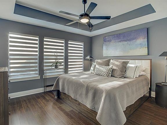 The primary bedroom on the second floor has a tray ceiling with a modern ceiling fan and wood floors.