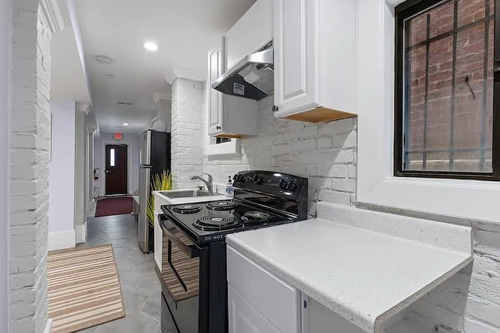 Efficient galley kitchen with ample white cabinetry, durable countertops, range with hood, and a window for ventilation.