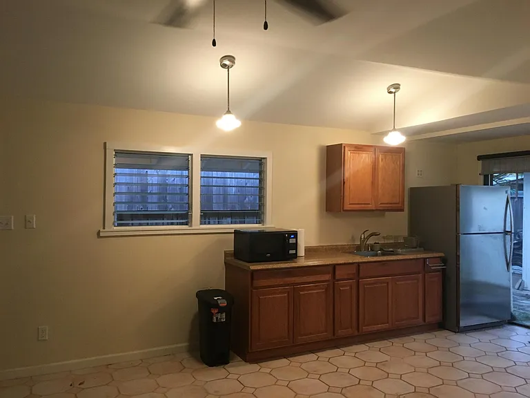 Full-size stainless-steel refrigerator and kitchenette with granite countertop and new wooden cabinets.