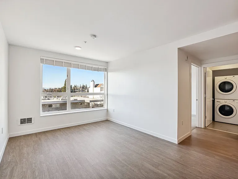 Bright, modern living room at 4400 Alaska in Seattle, WA, featuring stylish wood-look floors, large windows, and convenient in-unit stacked washer/dryer.