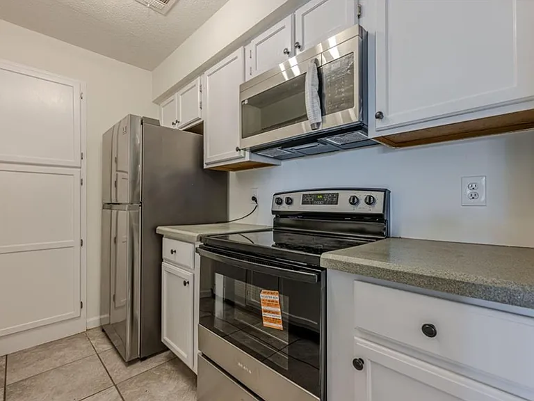 Kitchen featuring appliances with stainless steel finishes, a textured ceiling, white cabinetry, light tile patterned floors, and dark countertops
