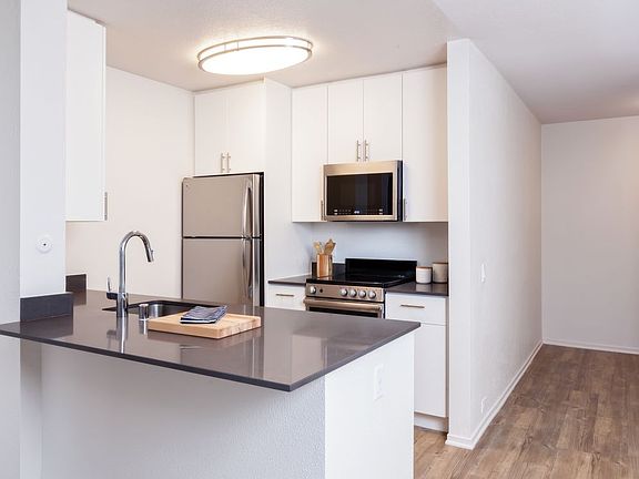 Kitchen with dark grey countertops, white cabinetry, stainless steel appliances and hard surface flooring