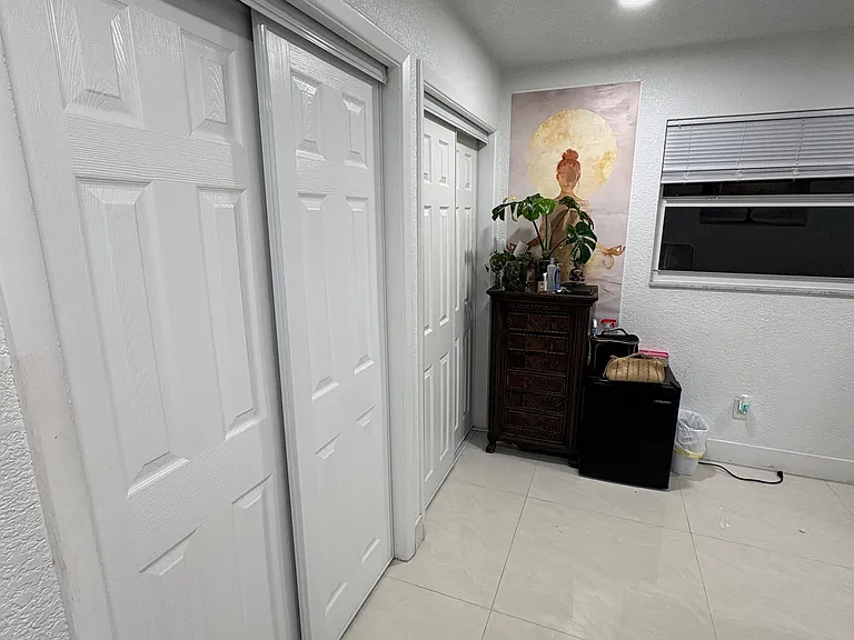 Narrow room corner with sliding closet doors, tile floor, a small dresser, wall art, and a window with blinds.