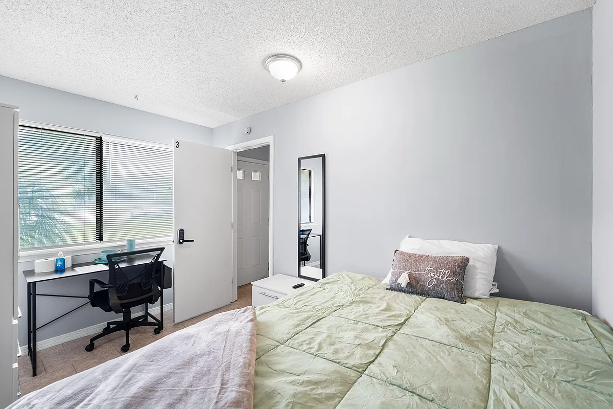 Furnished bedroom with a queen bed, wardrobe storage, wall-mounted TV, and a work desk beside a large window - Ponce De Leon Ave