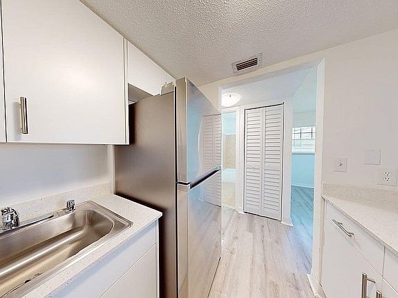 Modern kitchen with sleek stainless steel appliances, bright white cabinetry, and elegant wood flooring creating a fresh and inviting atmosphere.