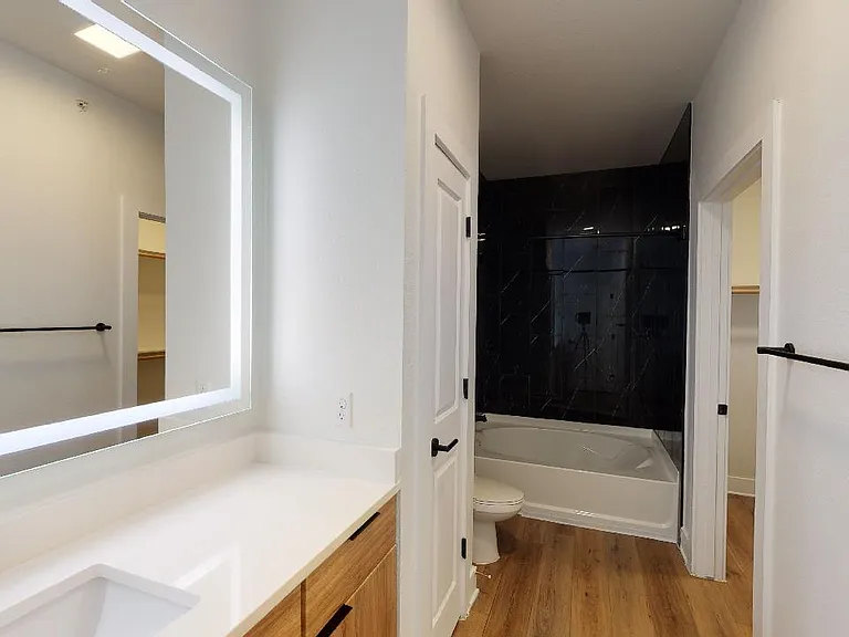 Apartment bathroom with large soaking tub, wood-style flooring and LED vanity mirror.