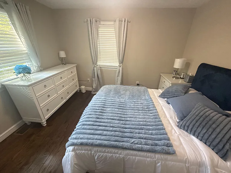 Furnished bedroom with a full bed, two dressers for storage, and window coverings for privacy and light control.