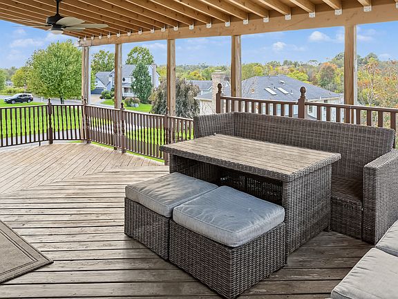 Spacious covered deck with ceiling fan and sweeping neighborhood and treetop views. Furnished with a wicker outdoor dining and lounge set, perfect for morning coffee, summer dinners, or relaxing rain or shine.
