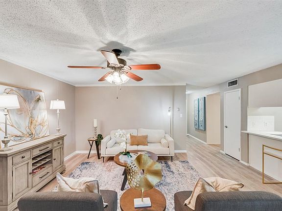 Living room with crown molding, ceiling fan, a textured ceiling, and light wood-type flooring