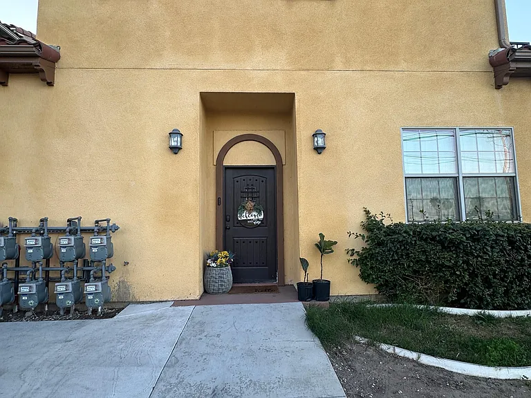 Stucco entry with covered doorway, exterior lighting, and a concrete walkway leading to the front door.