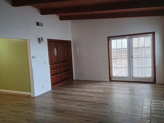 Built-in bookcase and French doors. Kitchen and dining area to the left.
