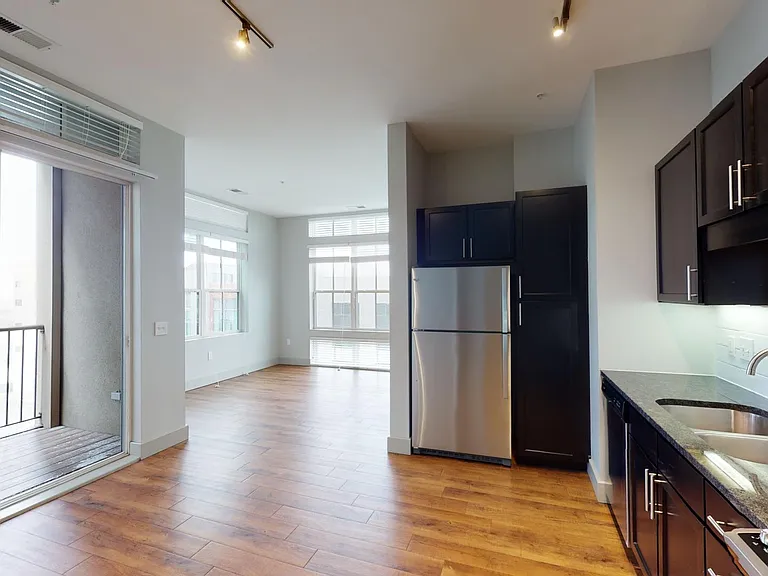 Apartment kitchen with stainless steel appliances, dining and living room with wood-style flooring.