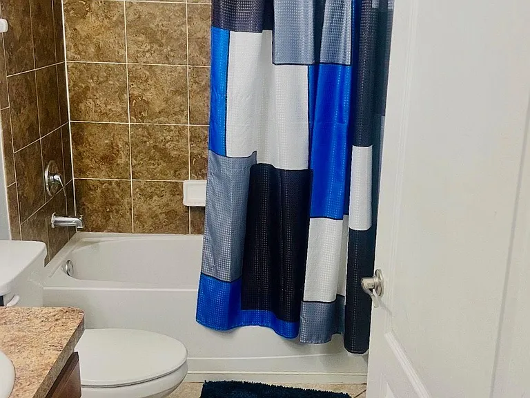 Full bathroom with tiled tub/shower surround, vanity with countertop, and durable tile flooring for easy maintenance.