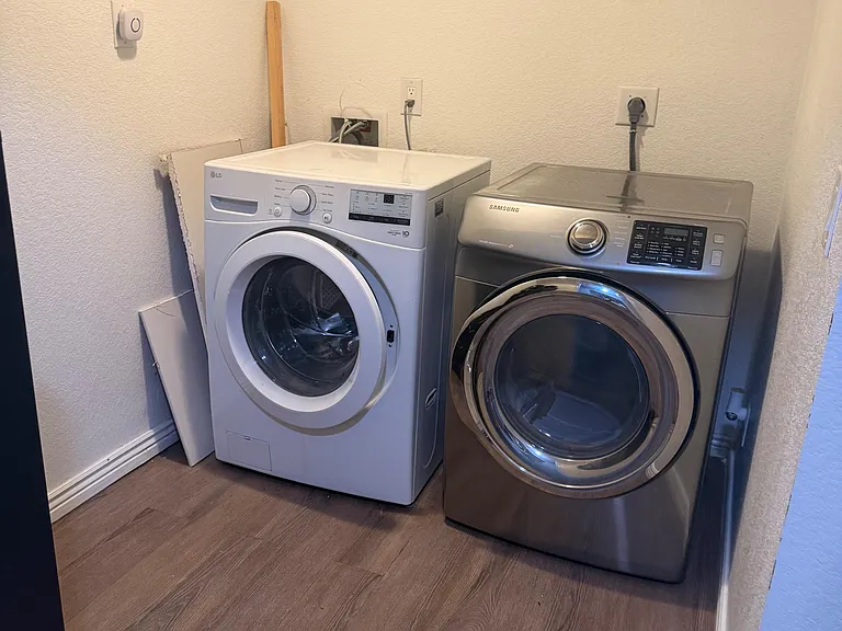 Dedicated laundry nook with full-size front-loading washer and dryer plus an overhead shelf for supplies.