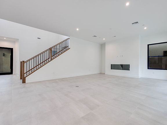 A spacious, minimalist interior with a wooden staircase, white walls, and a large open space.