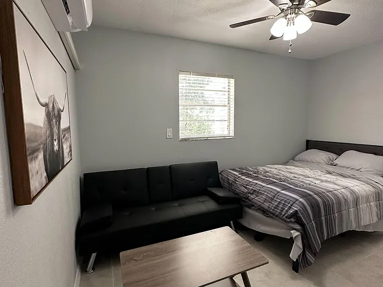 Furnished bedroom with a ceiling fan, window with blinds, tile flooring, and a seating area with a coffee table.