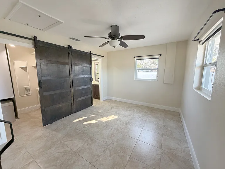 The master bedroom offers abundant natural light, a ceiling fan for comfort, and modern barn doors. (Angle 1)