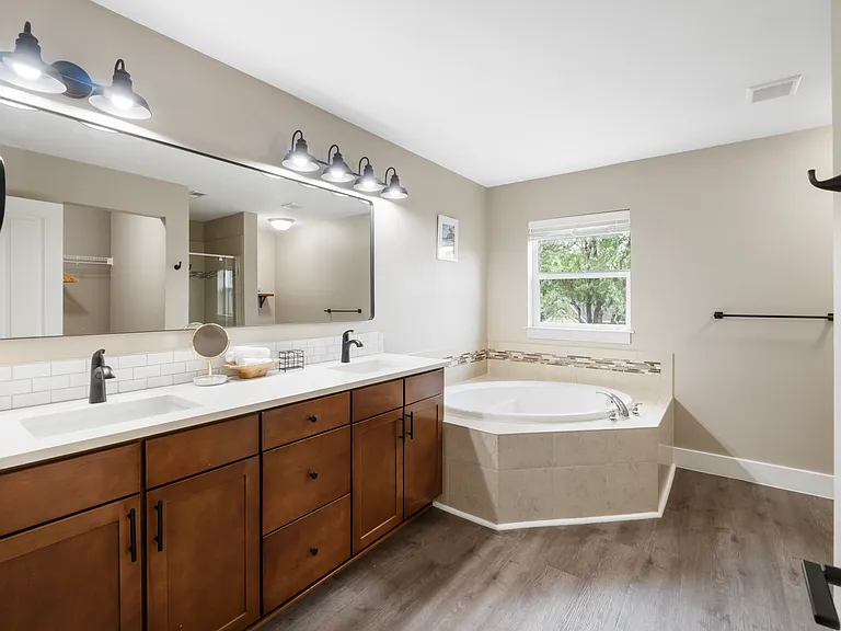 Primary bathroom has dual sinks, a tub, a toilet off to the right, and a stand up shower and walk in closet across from the sinks