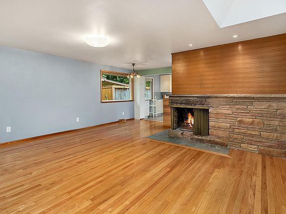 Living room includes a skylight and open floor plan. Mid-century stone corner fireplace and warm wood details.