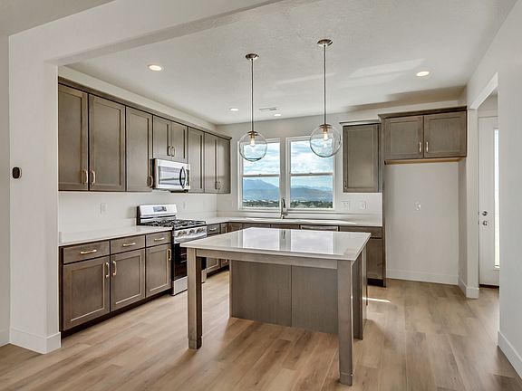 Modern kitchen with stainless steel appliances, a central island, and wood cabinetry. Large windows
