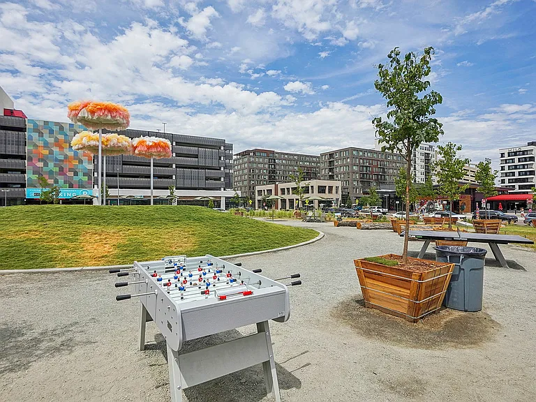 Vibrant urban park view featuring colorful sculptures, open green space, and recreational facilities, surrounded by modern apartment buildings.