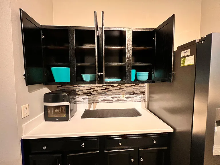 Kitchen storage and prep area with upper cabinets, mosaic tile backsplash, and ample counter space beside the fridge.