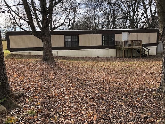 Tree filled corner lot with front deck and storage building.