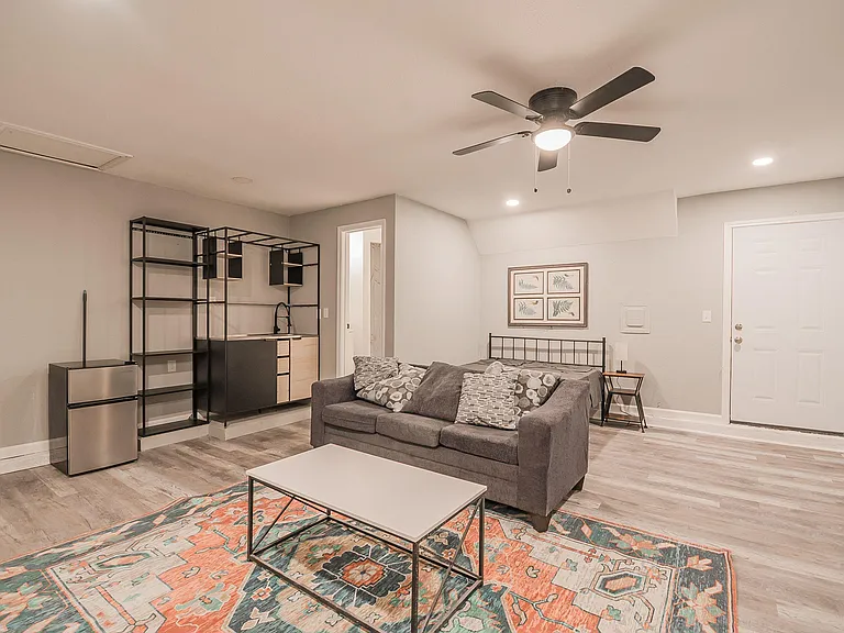 Open living area with durable flooring, ceiling fan lighting, and flexible space for lounging plus a compact kitchenette.