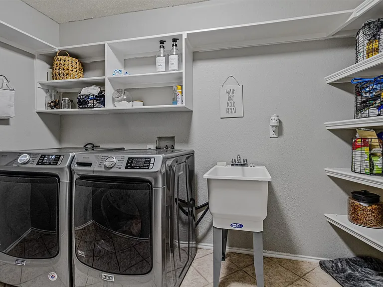 Dedicated utility space featuring a laundry sink with dual-handle faucet, built-in shelving, and a tiled floor