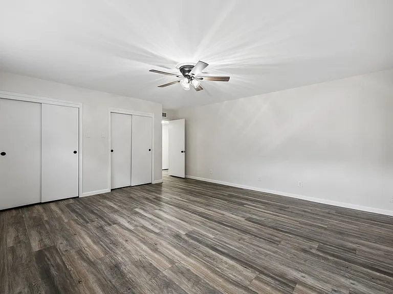 Spacious room featuring wood-finish flooring, a ceiling fan with light, and multiple sliding door closets