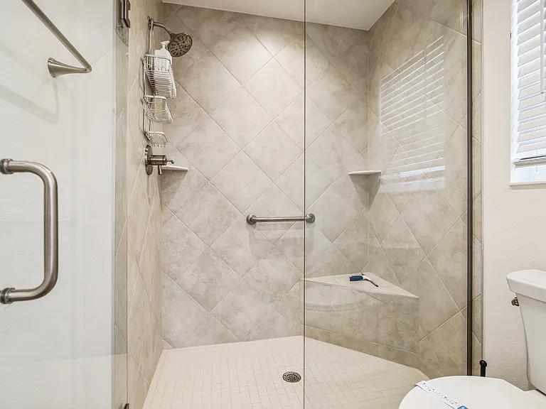 Beautiful Tiled Shower with Glass Doors, a Seating Area, and Handle Bar.