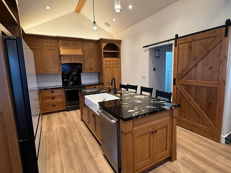 View of kitchen from living area with barndoor covering hallway entrance. Custom built oak cabinets.